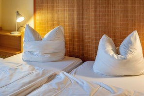 Une chambre d’hôtel avec deux lits, chacun équipé d’un oreiller, d’une lampe de chevet et d’une tête de lit en bois.