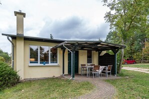 Un petit bâtiment doté d’un patio couvert, d’une cheminée et d’une voiture garée à proximité.