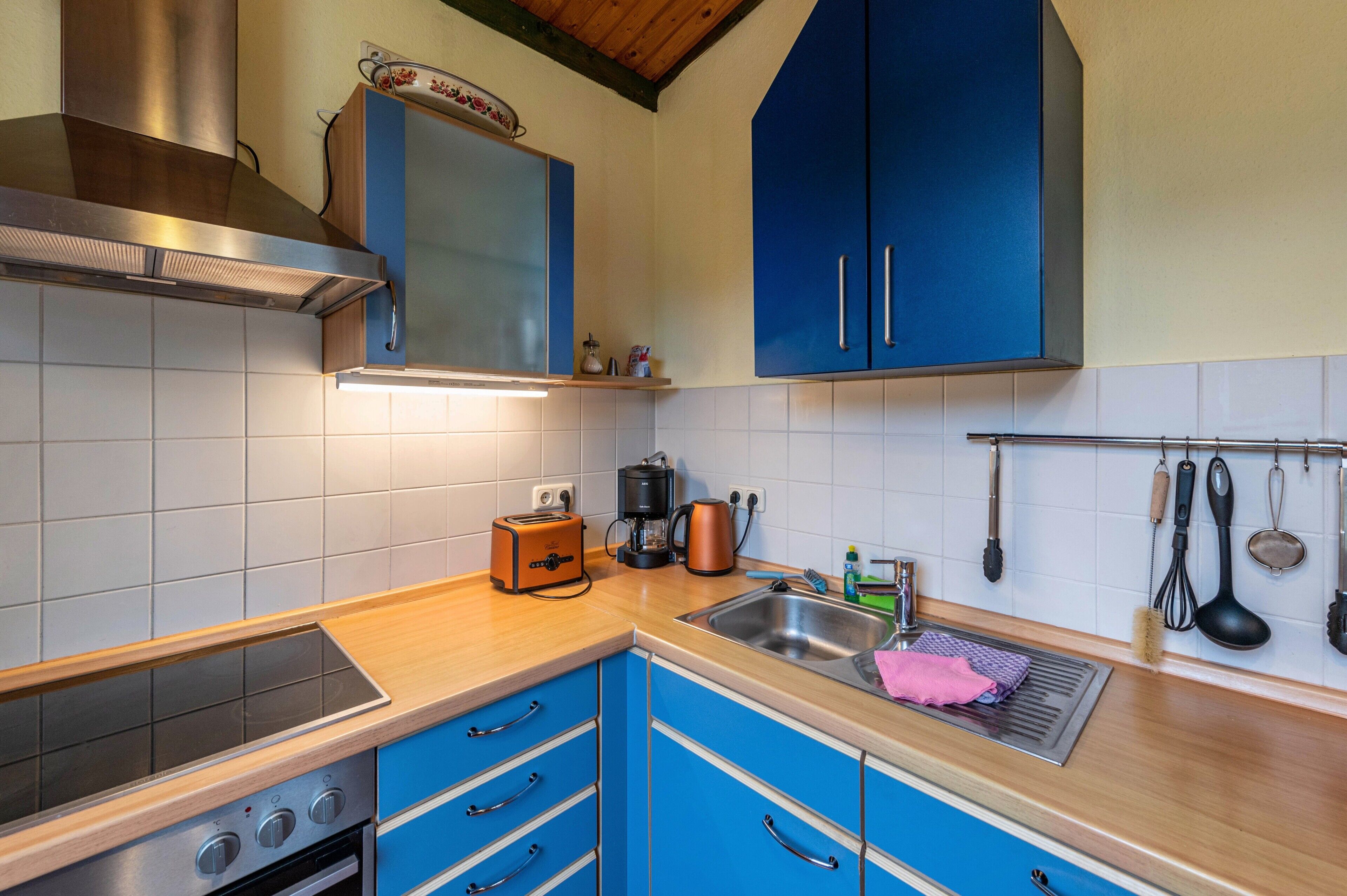 Una cucina con fornello, forno, pensili blu, cappa aspirante in acciaio inossidabile e un appendiabiti con utensili da cucina.