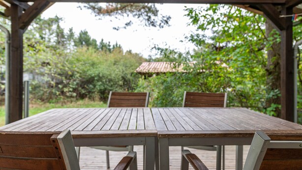 A wooden table with chairs under a wooden pergola, surrounded by greenery. - Holiday Home 'Ferienhaus Mine Hüsung' with Private Terrace, Shared Garden and Wi-Fi (Feldberger Seenlandschaft)