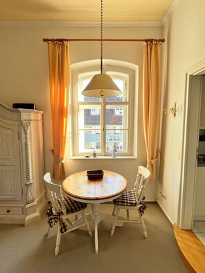 Et spiseområde med et rundt bord, to stole, en hængende lampe og et vindue med gardiner.