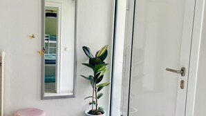 A hallway with a white door, a potted plant, a mirror, and a pink ottoman.