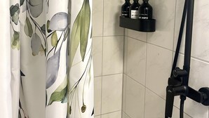 A shower area with a handheld showerhead, a black hose, and a shelf with two bottles of shampoo and conditioner.