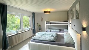 A bedroom with a bunk bed, a radiator, a window with curtains, and a green rug.