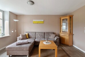Ein modernes Wohnzimmer mit einem grauen Ecksofa, einem Holztisch, einem Schrank und einer Stehlampe.
