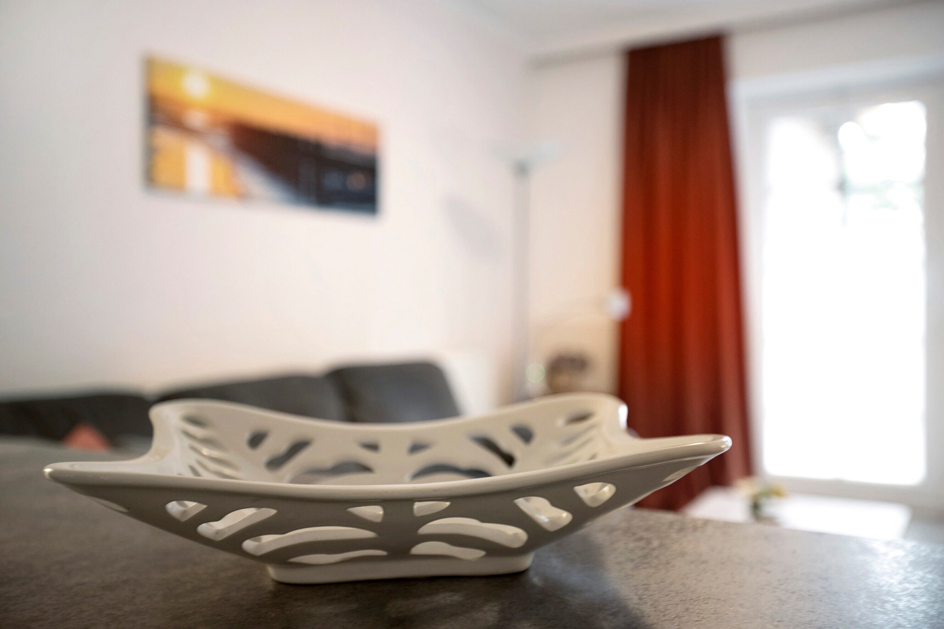 A white decorative bowl on a table in a room with a couch and a painting on the wall.