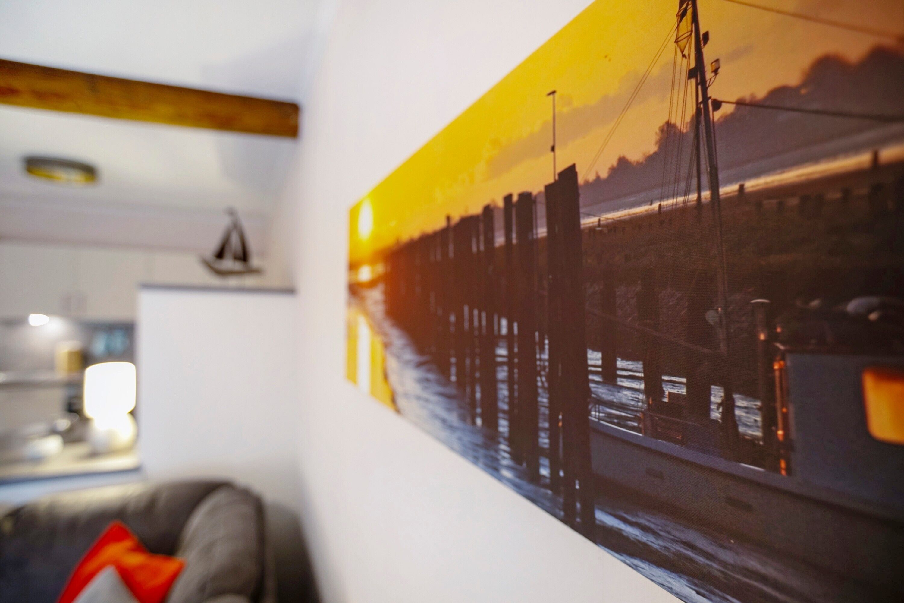 A wall with a framed picture of a sunset over a bridge.