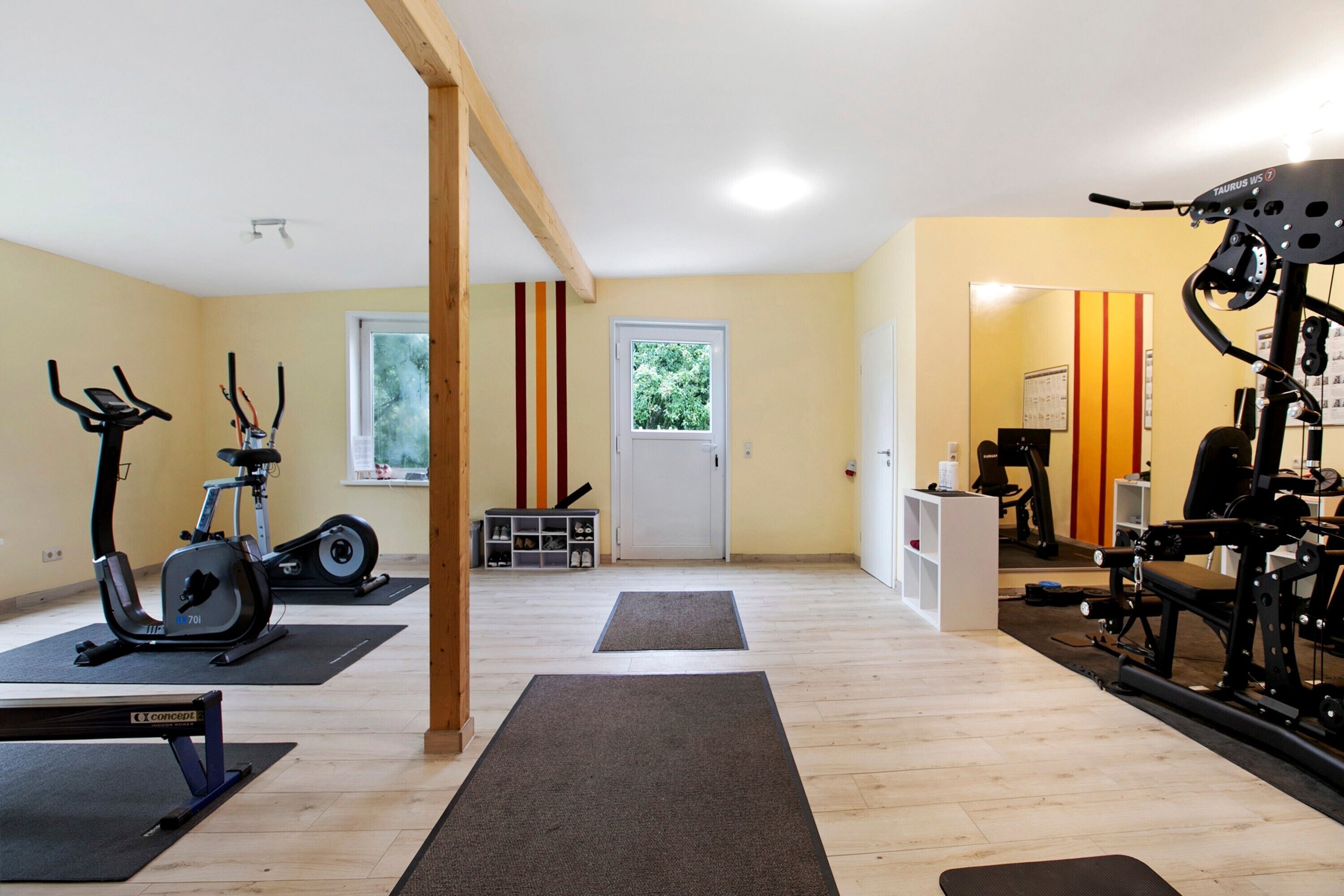 Een sportschool met trainingsapparatuur, matten en een houten balkenconstructie.