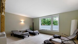 A room with two reclining chairs, a small table, a window with blinds, and a wall-mounted light fixture.