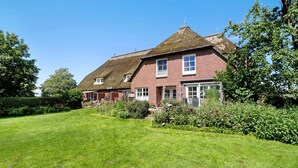 A large brick house with a thatched roof, surrounded by a well-maintained lawn and various plants.