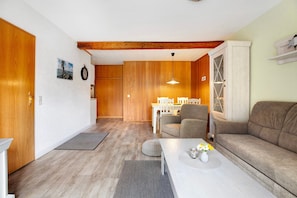 Uma sala de estar com sofá, mesa de centro com flores, espaço de jantar com cadeiras e teto de madeira.