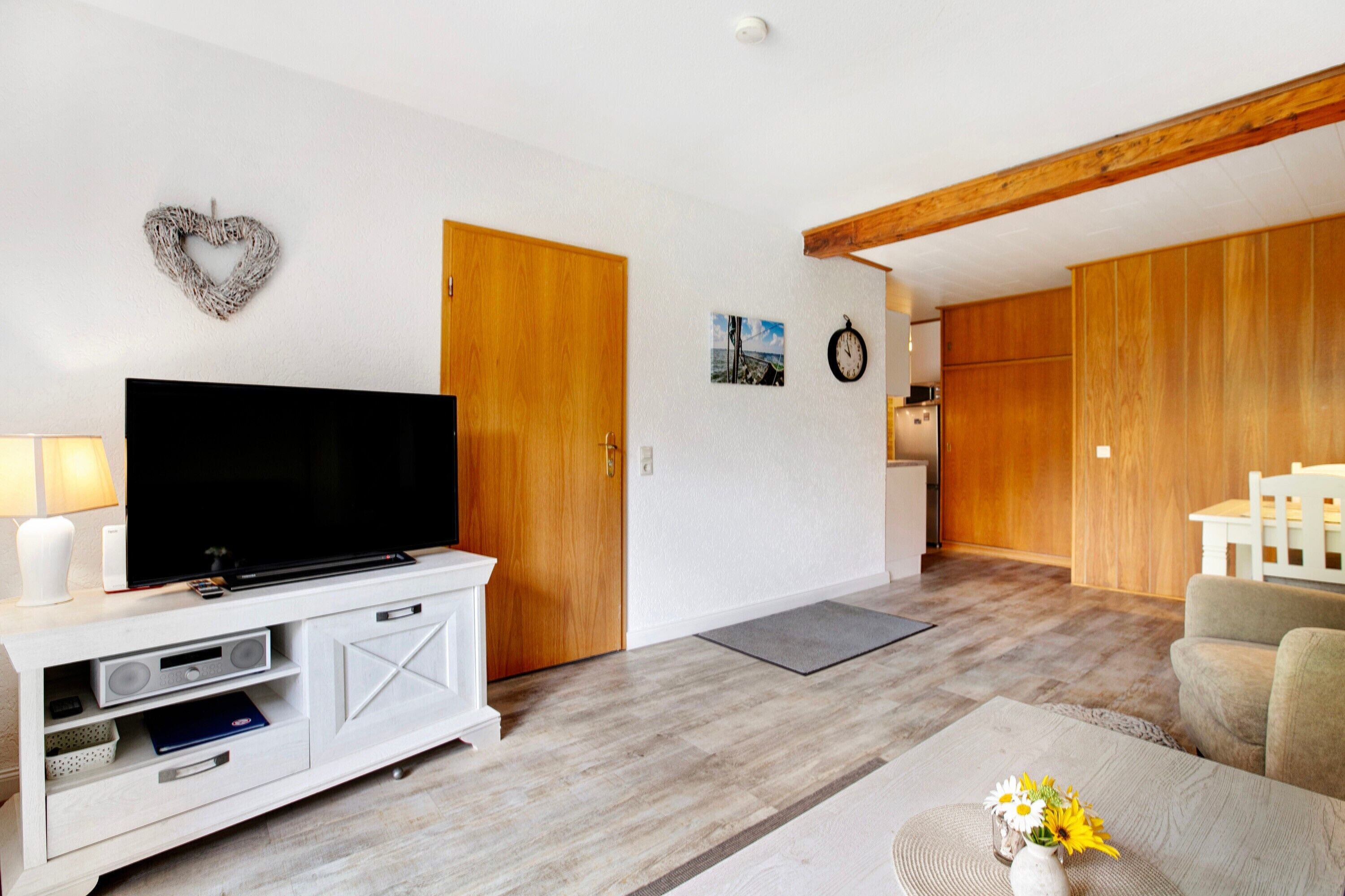 Ein Wohnzimmer mit einem Flachbildfernseher auf einer weißen Unterhaltungsecke, Holztüren, einer Wanduhr und einem kleinen Bild.