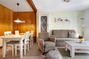 Uma sala de jantar com uma mesa e cadeiras brancas, uma poltrona bege e um sofá branco, além de uma mesa de centro branca com um vaso.