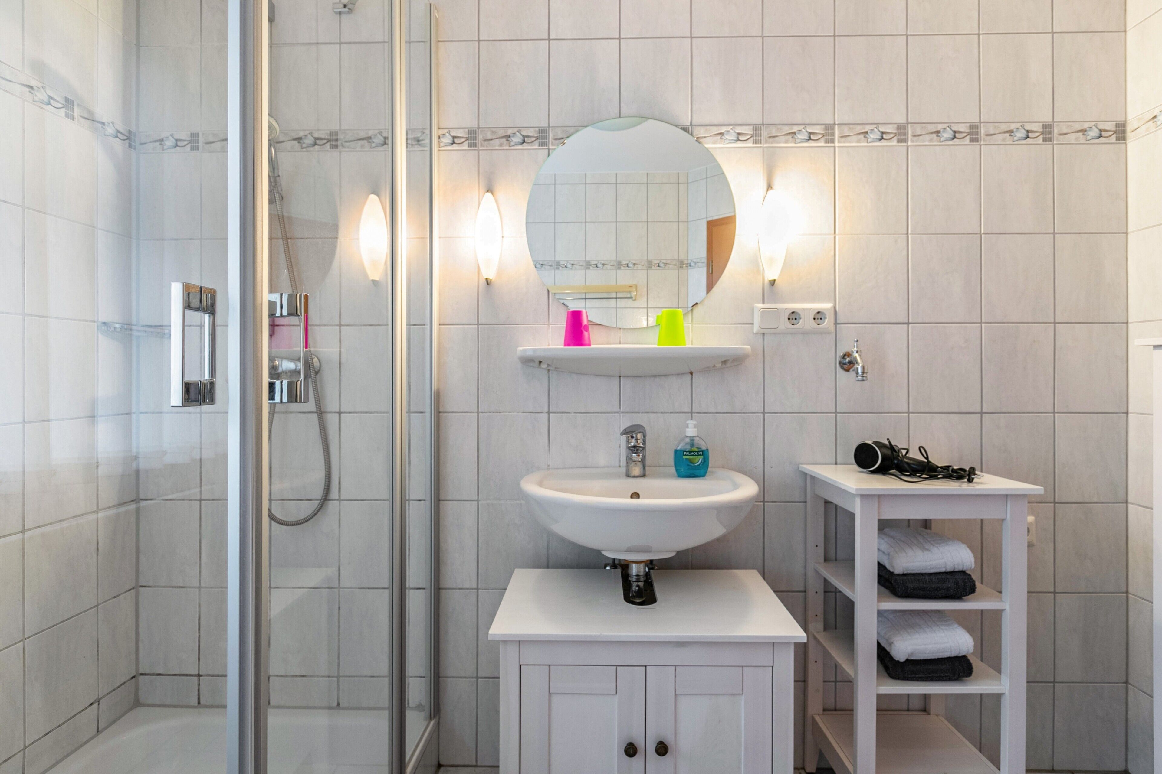 A bathroom with a shower, a sink, a mirror, and a shelf with towels.