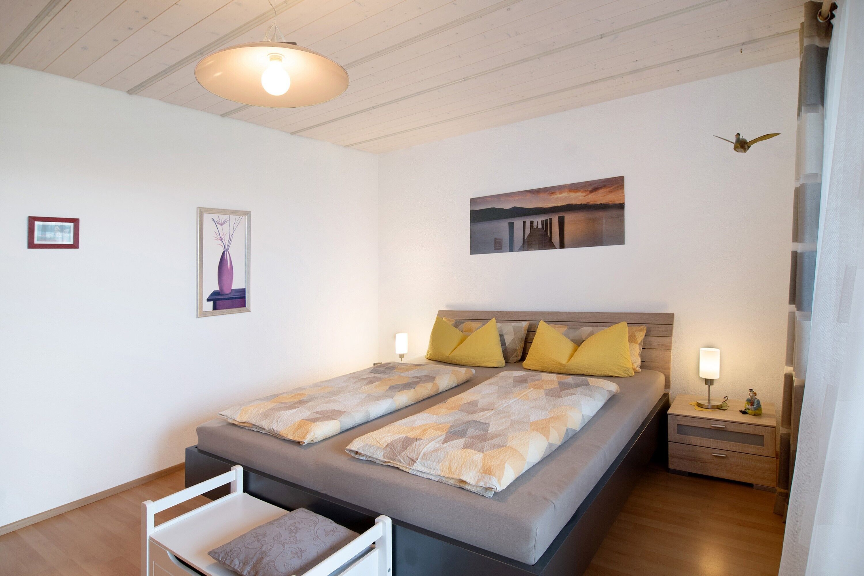 A double bed with a headboard, two bedside tables with lamps, a small chair, and a wall-mounted picture.