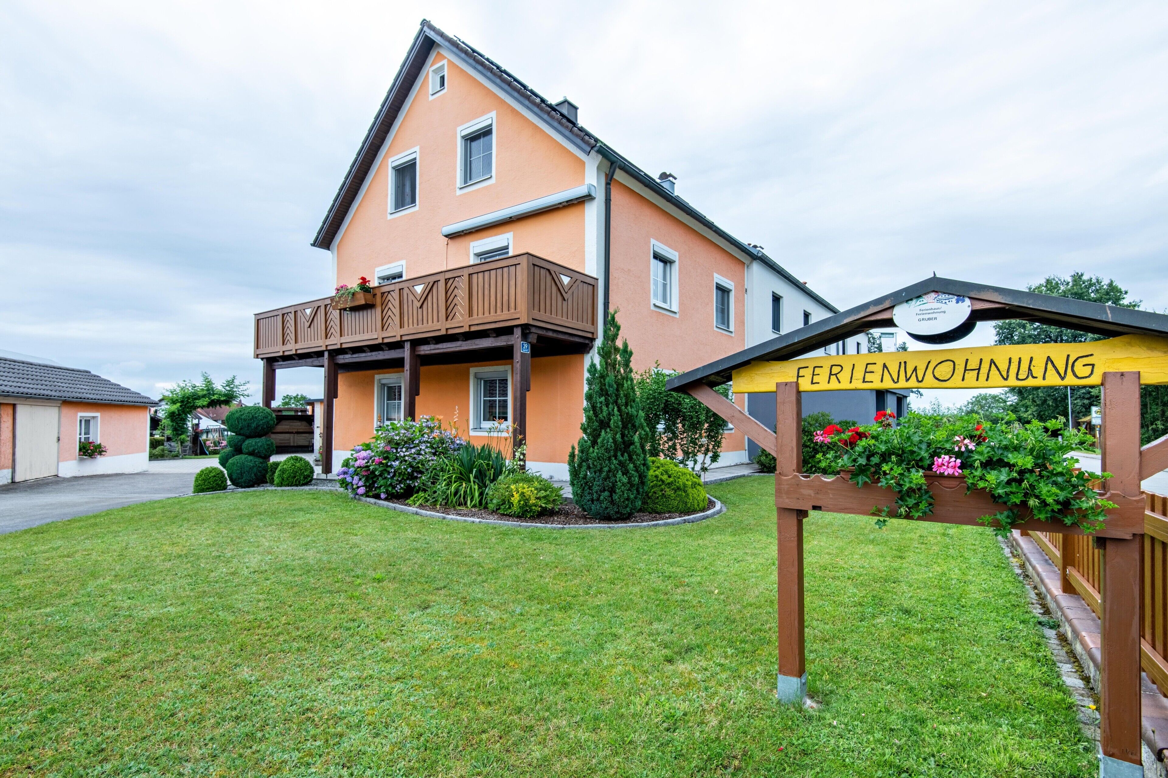 Ein zweistöckiges Gebäude mit Balkon, einem Schild mit der Aufschrift 'FERIENWOHNUNG' und gepflegter Bepflanzung.