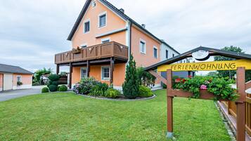 Ein zweistöckiges Gebäude mit Balkon, einem Schild mit der Aufschrift 'FERIENWOHNUNG' und gepflegter Bepflanzung.