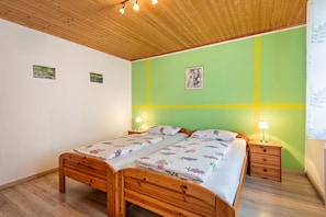 Ein Doppelbett mit floraler Bettwäsche, ein hölzerner Kopfteil, zwei Nachttische mit Lampen, eine grüne Akzentwand und eine Holzbalkendecke.