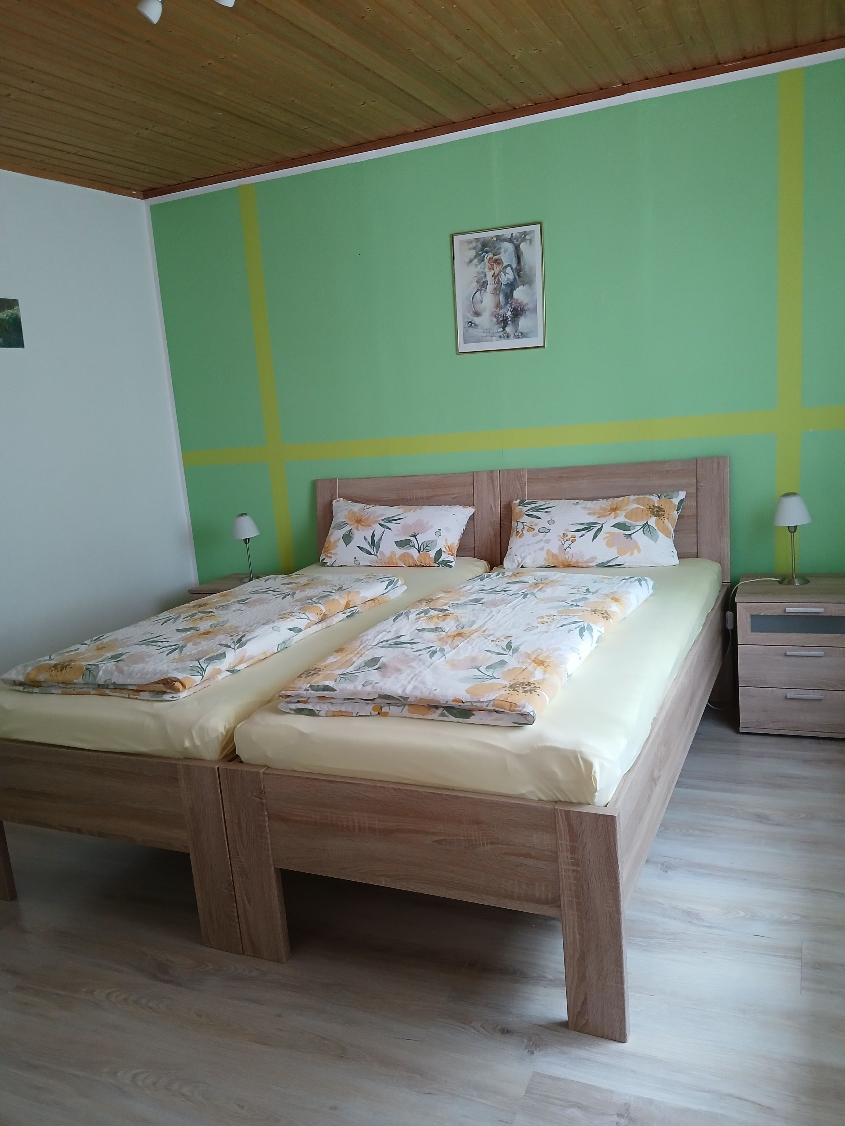 Una habitación con una cama de madera, paredes verdes, un cuadro y una mesita de noche con lámpara.