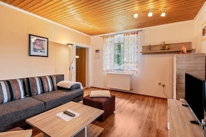 Ein Wohnzimmer mit einer Couch, einem Couchtisch, einem Fernsehschrank, einer Heizung und einem Fenster mit Vorhängen.