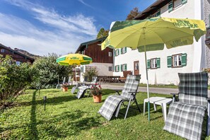Espace extérieur aménagé avec des parasols, un bâtiment aux volets verts et une pelouse.