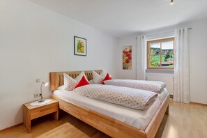 Une chambre à coucher avec un lit en bois, du linge de lit blanc, des oreillers rouges, une table de chevet avec une lampe et une fenêtre donnant sur un paysage verdoyant.