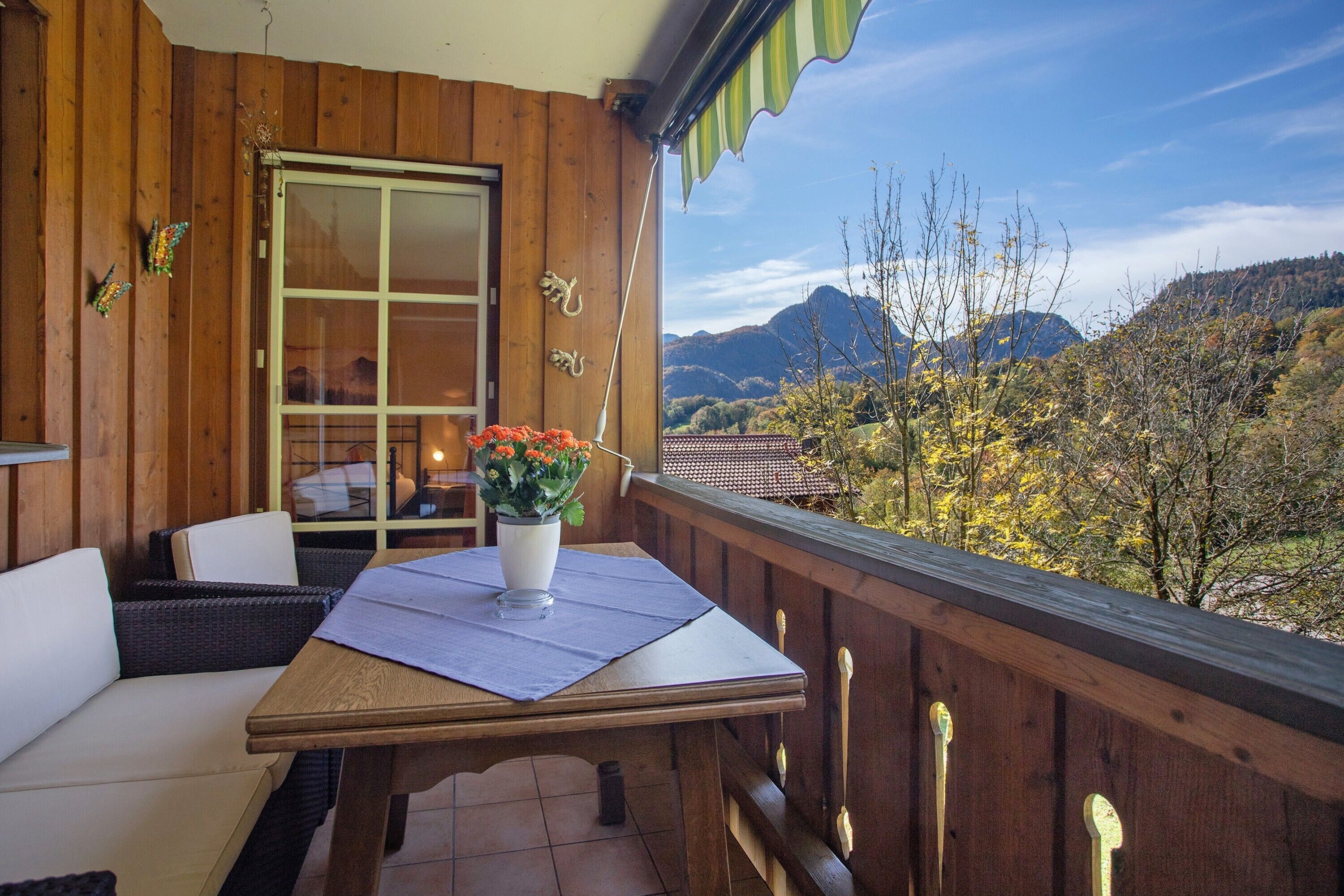A wooden balcony with a table, chairs, and a potted plant.