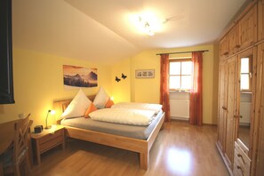 Une chambre à coucher comprenant un lit, une table de chevet, une lampe, une armoire en bois et une fenêtre avec des rideaux.