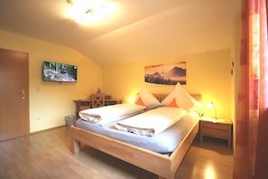 Un dormitorio con una cama, un televisor montado en la pared, un escritorio con una silla y un cuadro sobre la cama.
