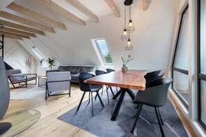 A modern loft with exposed wooden beams, a dining area with a wooden table and chairs, and large windows offering views. - Apartment 'Penthouse Kokorey' with Shared Garden, Balcony and Wi-Fi (Halstenbek)