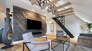 Un loft moderno con pared de piedra, chimenea, televisor y escalera.