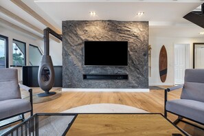 Una sala de estar moderna con una pared de piedra, un televisor montado, una chimenea y dos sofás grises.