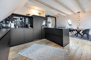 A modern kitchen with dark cabinetry, a built-in oven, and a large island with seating. - Apartment 'Penthouse Kokorey' with Shared Garden, Balcony and Wi-Fi (Halstenbek)