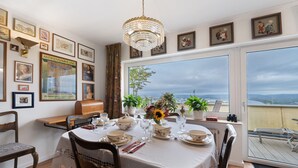 A dining area with a table set for four, a chandelier, and a view of the city through large windows. - Apartment 'Rheinblick Am Rheinsteig' with Mountain View, Wi-Fi and Air Conditioning (Urbar)