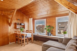 Ein Holzinnenraum mit Esstisch, Stühlen, einer Couch und großen Fenstern.