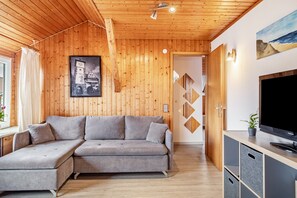 Un salon moderne avec un canapé d’angle, des murs en bois, un téléviseur à écran plat et un tableau représentant un château.