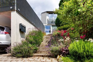 A residential building with a staircase leading to a door, surrounded by various plants and flowers.