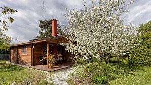 A wooden cabin with a covered porch, a chimney, and a blooming tree. - Holiday Home 'Blockhütte' with Private Terrace and Private Garden (Fürstenwalde/Spree)