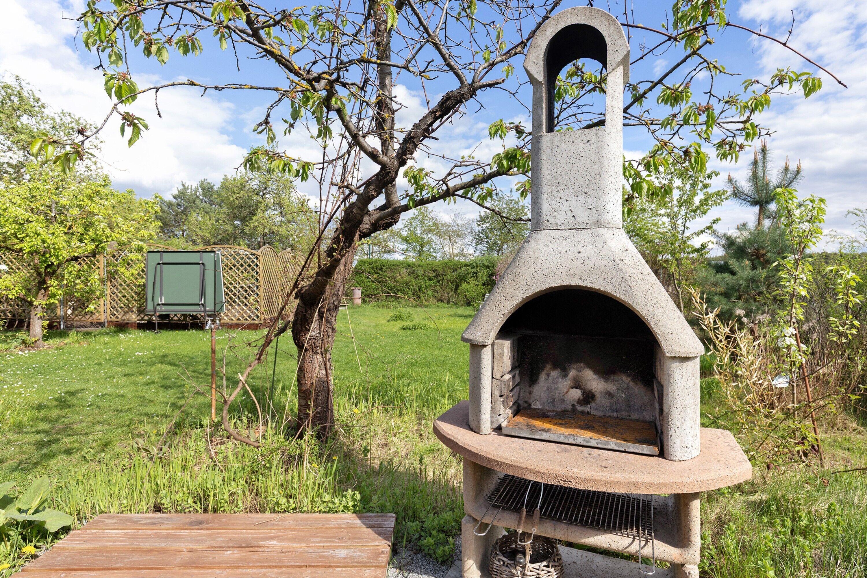 A stone outdoor oven with a chimney, surrounded by a grassy area and trees.
