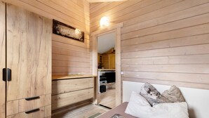 A wooden-paneled bedroom with a bed, a wardrobe, and a small kitchenette visible through an open door. - Holiday Home 'Blockhütte' with Private Terrace and Private Garden (Fürstenwalde/Spree)