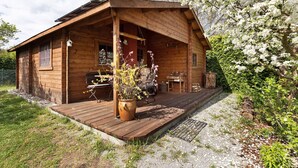 A wooden cabin with a porch, a large flower pot, and a grill area. - Holiday Home 'Blockhütte' with Private Terrace and Private Garden (Fürstenwalde/Spree)