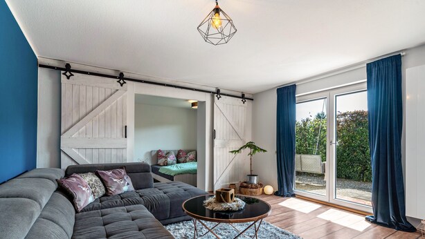 A modern living room with a sectional sofa, a coffee table, and a sliding barn door leading to a garden.