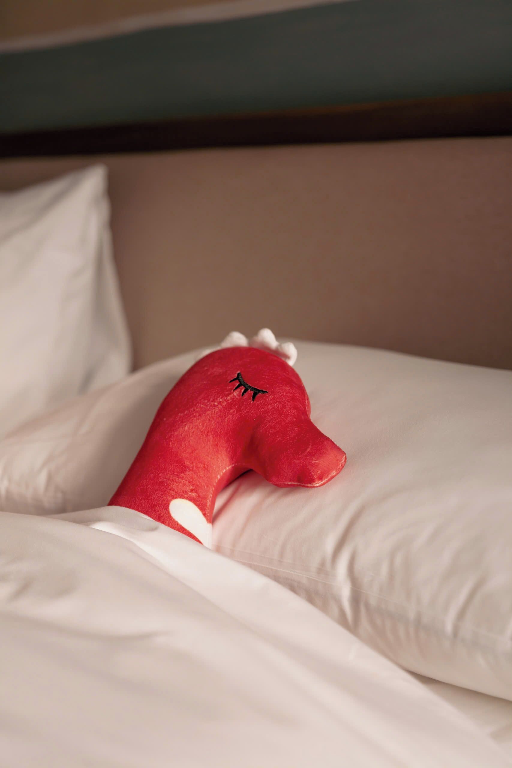 A bed with white bedding and a red plush toy.