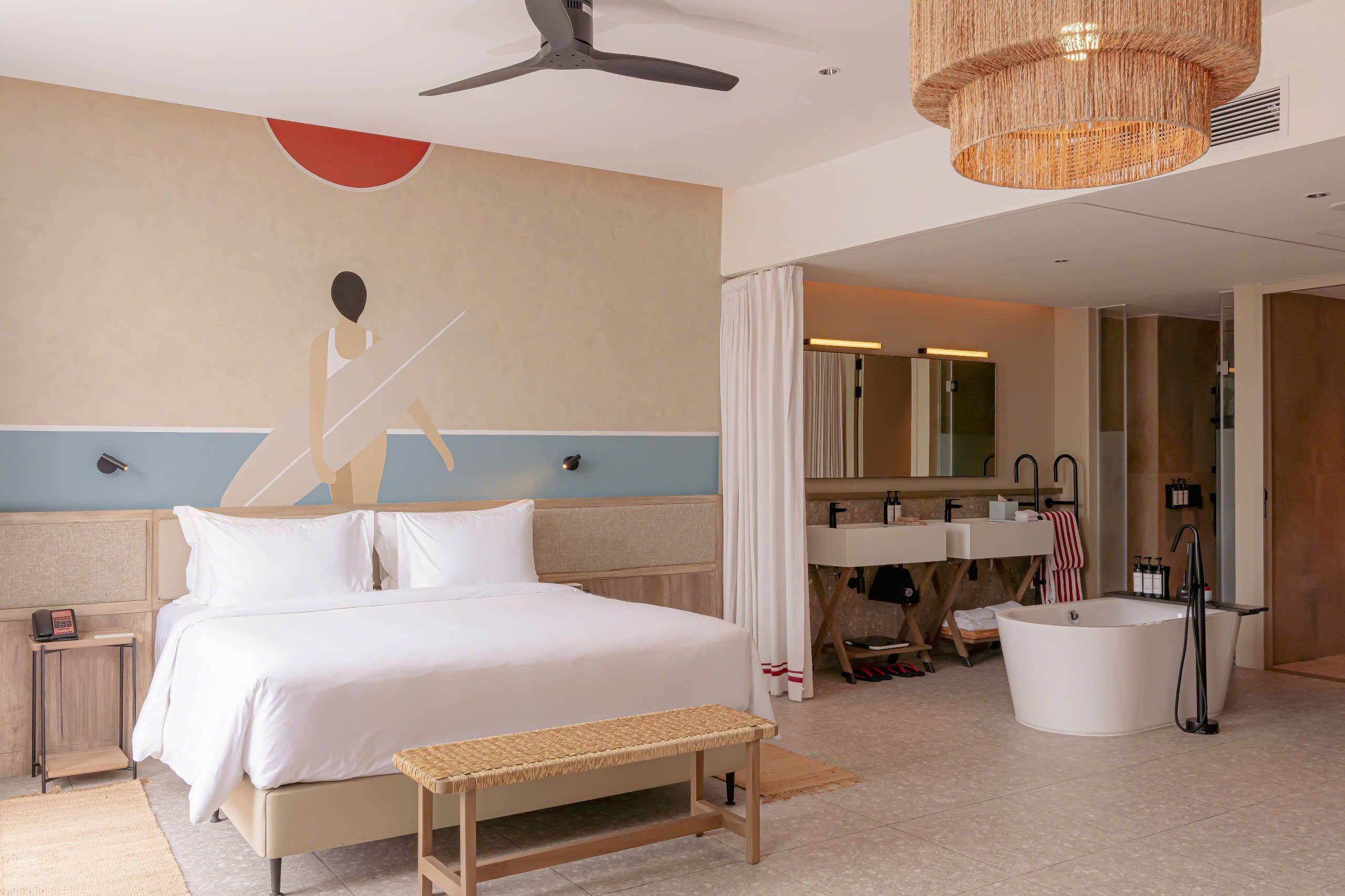 A hotel room with a bed, bedside table, bench, and a large mirror.