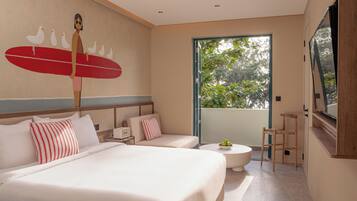 A hotel room with a large bed, a small sofa, a round coffee table, and a view of greenery through a large window.