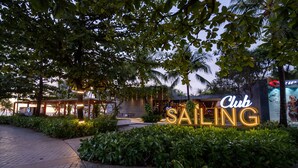 A well-lit outdoor area with a sign for 'Sailing Club' surrounded by lush greenery and a paved walkway.