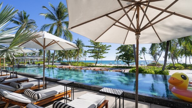 A poolside area with lounge chairs, umbrellas, and a view of the ocean.