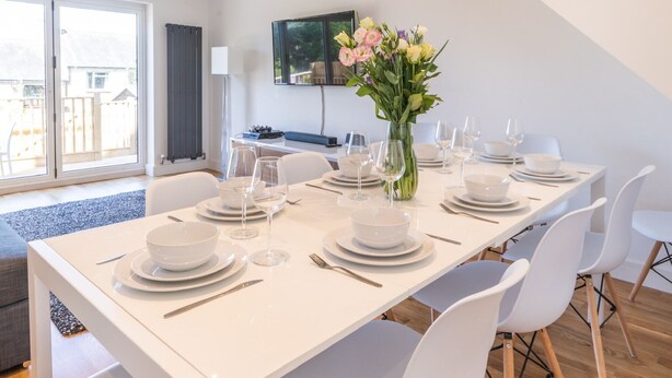 Un espace repas moderne avec une table blanche dressée pour six personnes, entourée de chaises blanches.