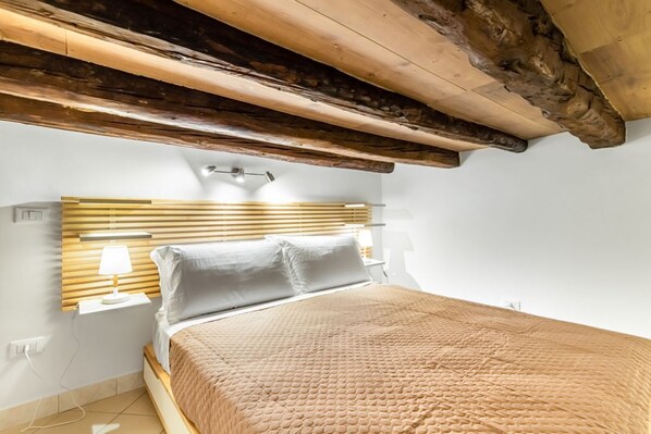 A bedroom with a wooden headboard, a bed with a textured blanket, bedside lamps, and a sloped ceiling.