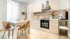 A modern kitchen with a dining area, featuring light wood cabinetry, a built-in oven, and a small dining table with chairs. - GuestHost - Modern Two-Levels Apartment with Balconies! (Palermo)